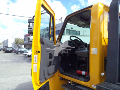 Truck cab interior and open door of a yellow 2019 International 4300 rollback truck showing steering wheel, dashboard, and driver seat area.