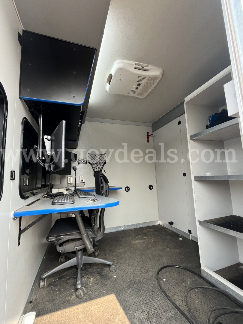 Ford Econoline interior showing workspace with computer, chair, storage shelves, and ceiling mounted device.