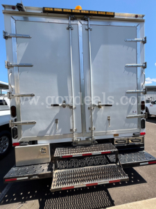 Ford Econoline box truck rear view showing two tall metal doors with latches, rear step bumper, and safety lights on top.