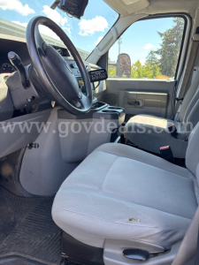 Front interior view of a 2017 Ford Econoline cab showing steering wheel, dashboard, and gray cloth driver seat with minor wear.