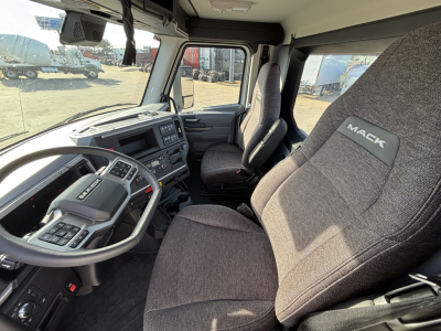 Truck cab interior with steering wheel and Mack-branded seat. Dashboard and driver's seat visible, gray fabric seats with Mack logo on headrest.