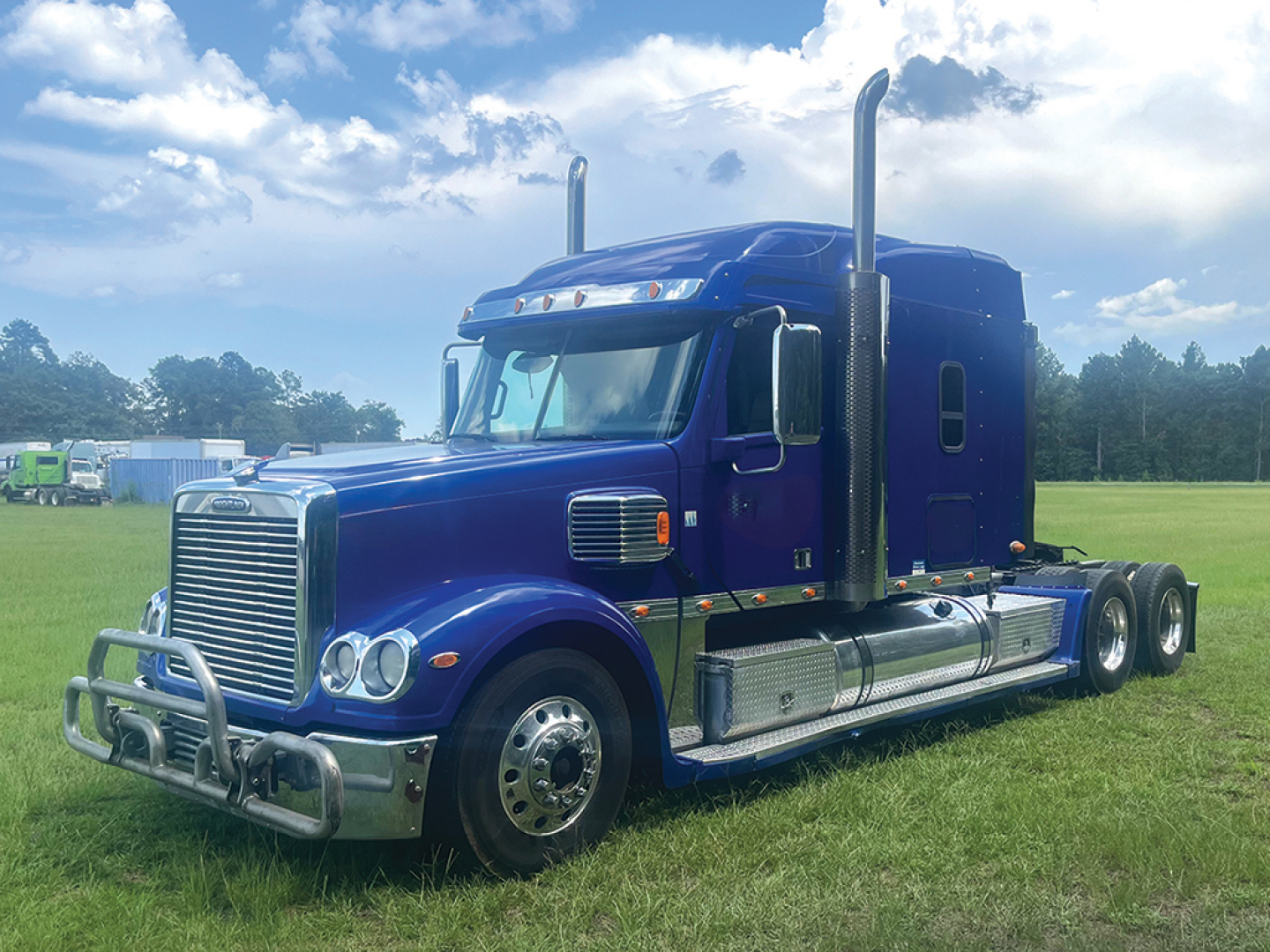 Blue 2018 Freightliner Coronado semi-truck tractor side view, showing chrome grille, sleeper cab, and dual rear axles.