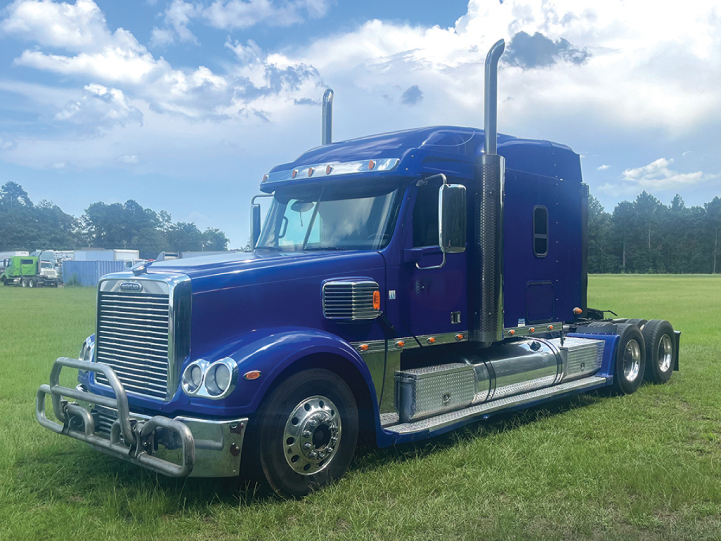 Blue 2018 Freightliner Coronado semi-truck tractor side view, showing chrome grille, sleeper cab, and dual rear axles.