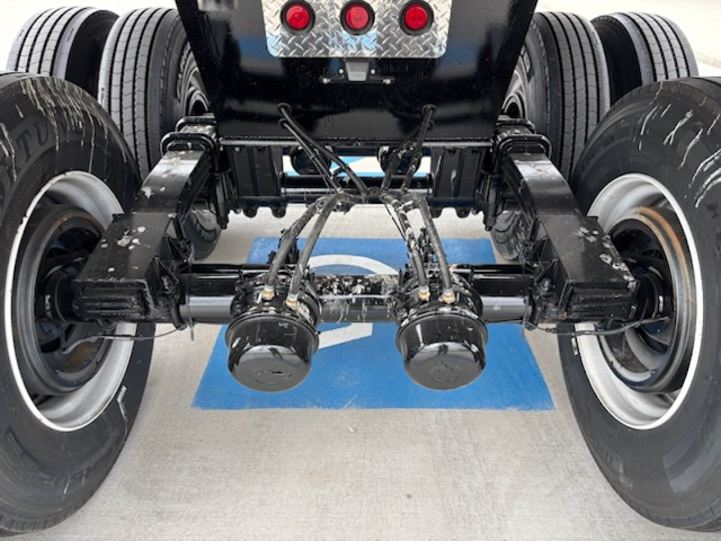 Trailer rear axle assembly showing dual axles, suspension, brake drums, and leaf springs under a dump trailer chassis.