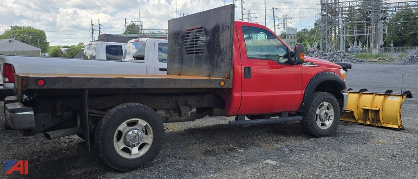 Red Ford F-250 Super Duty flatbed truck with a yellow front snow plow attachment, side tool box, in a lot.
