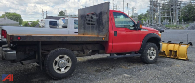 Red Ford F-250 Super Duty flatbed truck with a yellow front snow plow attachment, side tool box, in a lot.