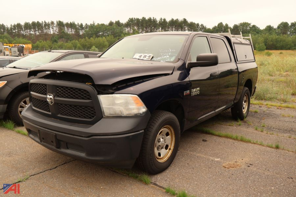 Ram 1500 pickup truck with cap, dark blue, front-left view. Badge on grille, RAM emblem, dual cab, pickup bed with cap. Plate area and front bumper visible.