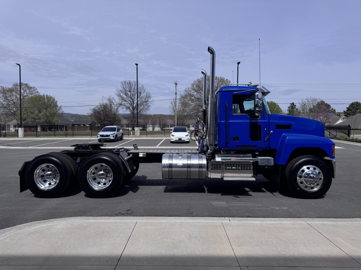 Conventional Daycab truck in blue cab with chrome tanks and dual rear axles, side view showing fuel tanks and exhaust stacks.