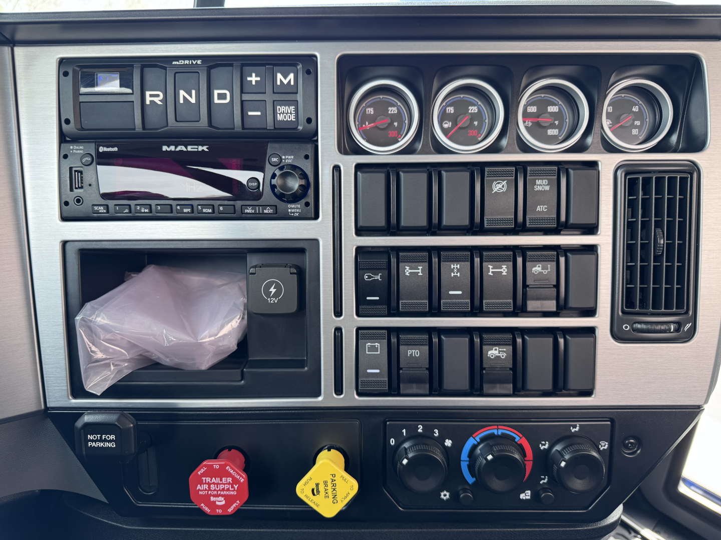 Mack truck cab interior dashboard with gauges, switches, and vents; visible text includes DRIVE MODE, MACK, and various control labels.