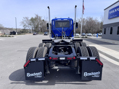 Truck chassis rear view showing dual rear axles and mud flaps with Bruckner's Truck & Equipment logo, blue cab, dealership lot.
