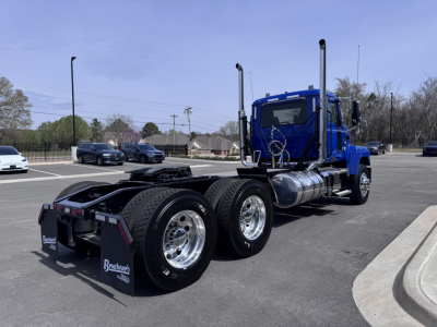 Blue 2027 Mack PI64T conventional daycab tractor rear/side view showing dual rear axles, chrome fuel tanks, and tall exhaust stacks. VIN 1M1PN4GYXVM021067.