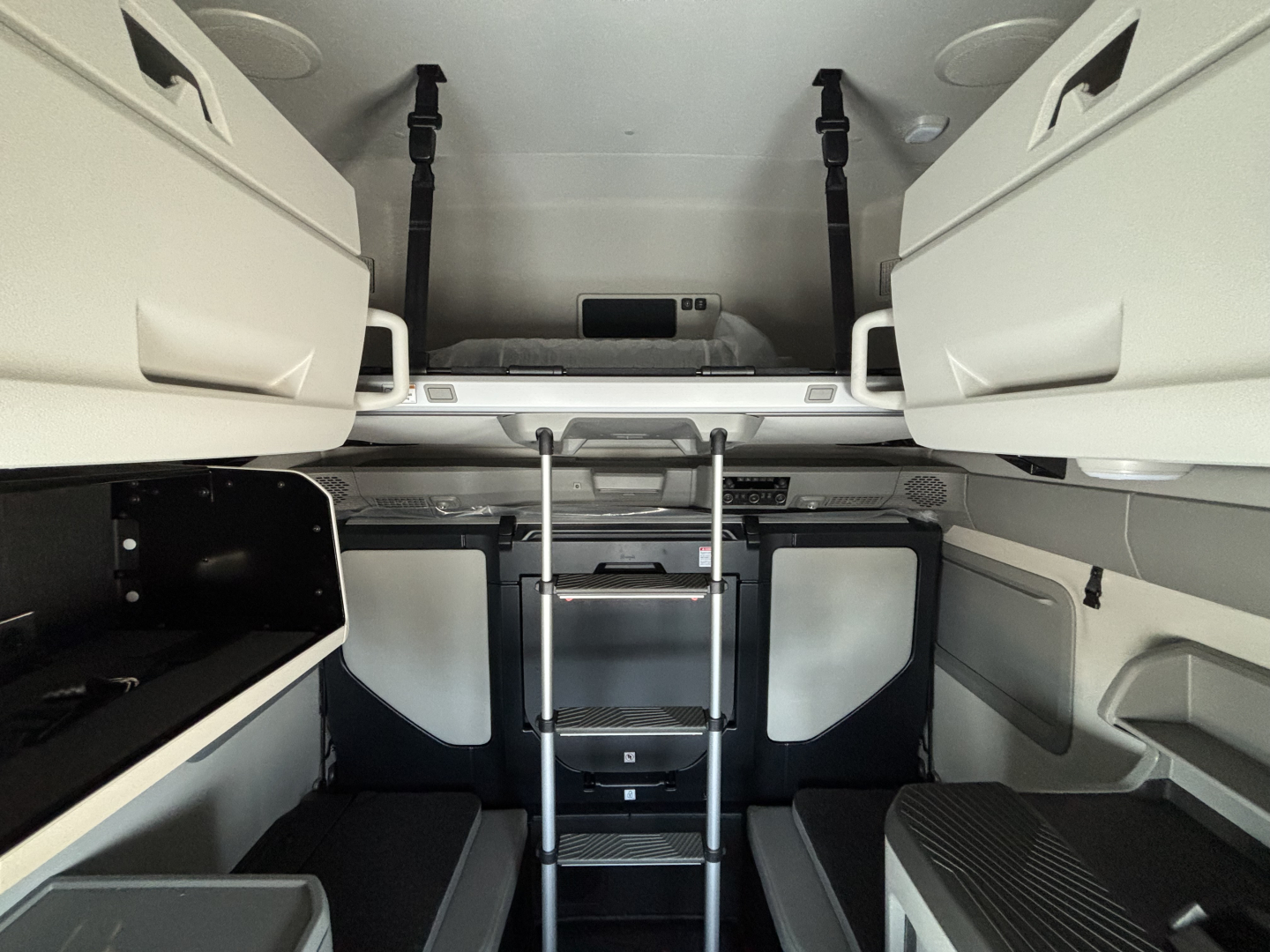 Interior view of a new Volvo VNL64T860 sleeper cab showing upper bunk area with ladder and storage compartments.
