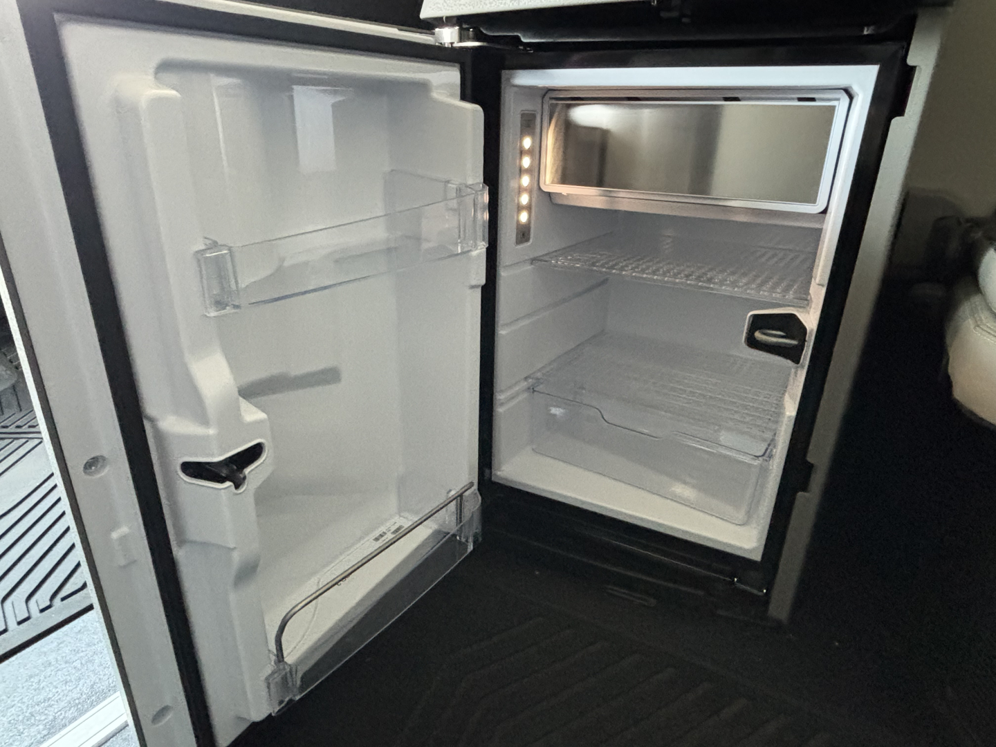  Volvo VNL64T860 cab interior showing open refrigerator/freezer unit and empty mini-bar area in the sleeper compartment.