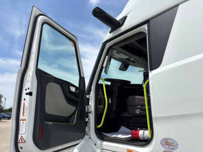 Truck cab interior with open door showing Volvo VNL64T860 sleeper, bright yellow handrails, folding steps, and dashboard visible.