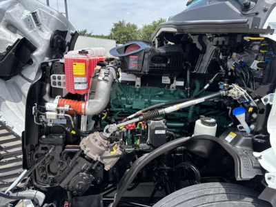 Engine bay of a Volvo VNL64T860 truck showing green engine, hoses, orange turbo component, coolant reservoir, wiring harness, and metallic frame.