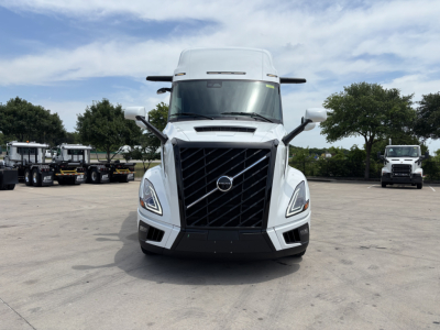 Front view of a white 2027 Volvo VNL64T860 truck with prominent black grille, large windshield, and side mirrors; dealership lot in background.