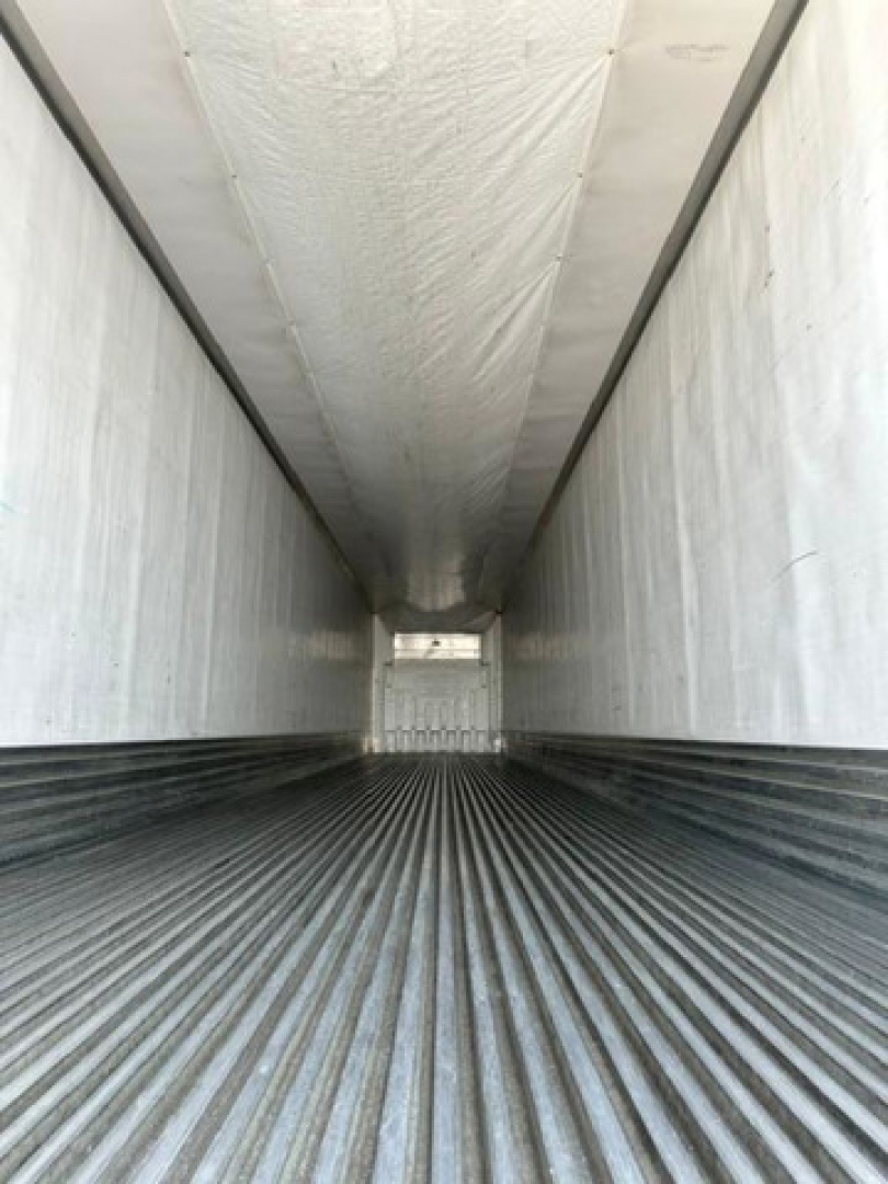 Interior of a refrigerated trailer with ribbed steel floor and white insulated walls, long narrow cargo area.