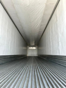 Interior of a refrigerated trailer with ribbed steel floor and white insulated walls, long narrow cargo area.