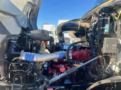 Engine bay of a 2022 Mack AN42T in-service showing red engine, blue hoses, wiring, and surrounding components.