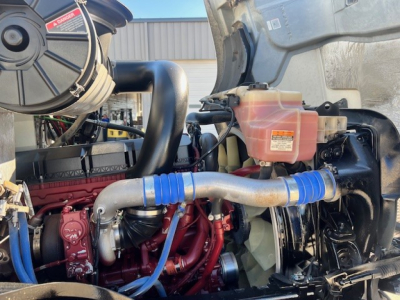 Engine bay of 2022 Mack AN42T with visible cooling system, hoses, and battery area.