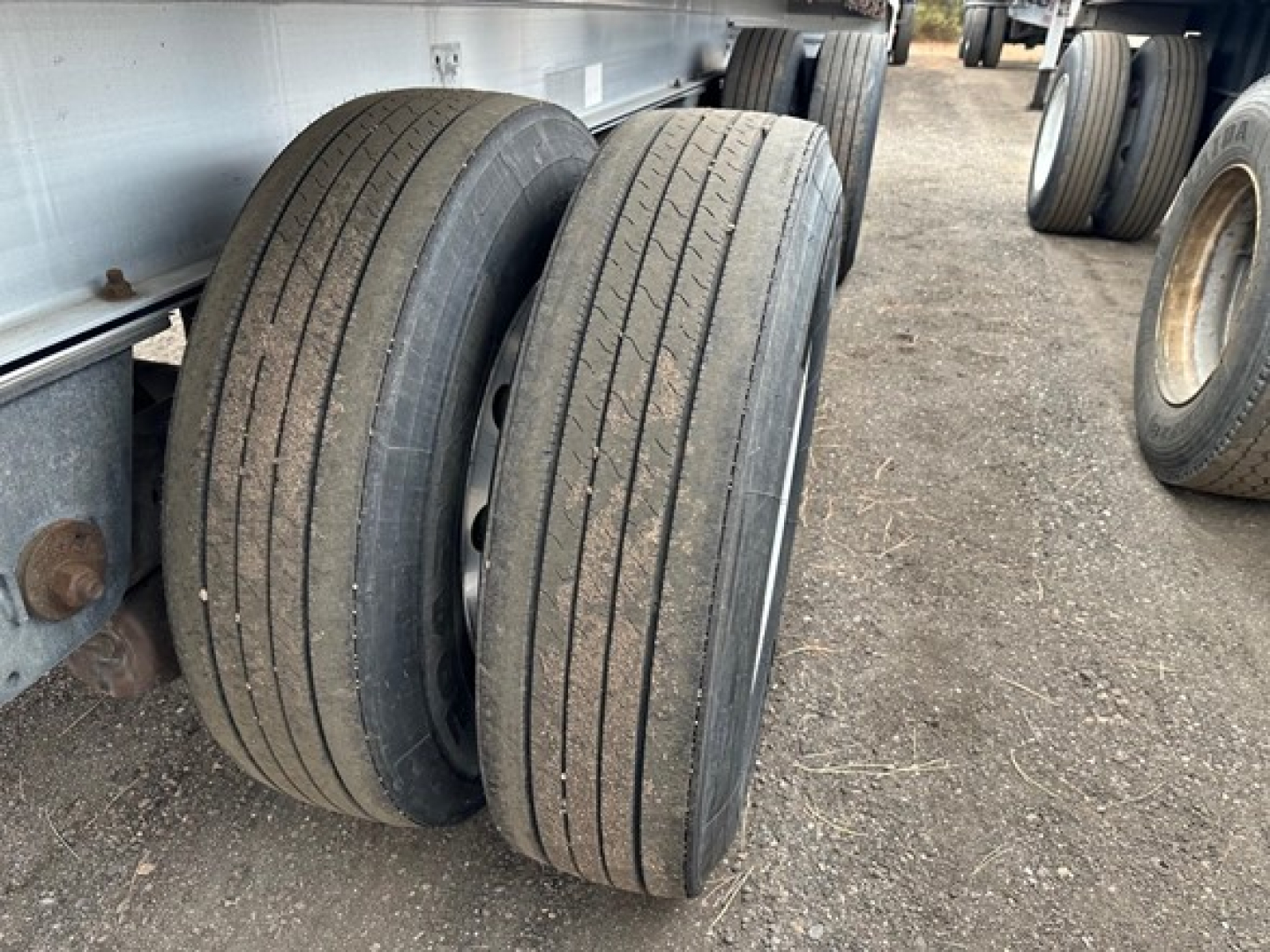 Two rear Mac trailer tires under a flatbed trailer with other tires in the background.