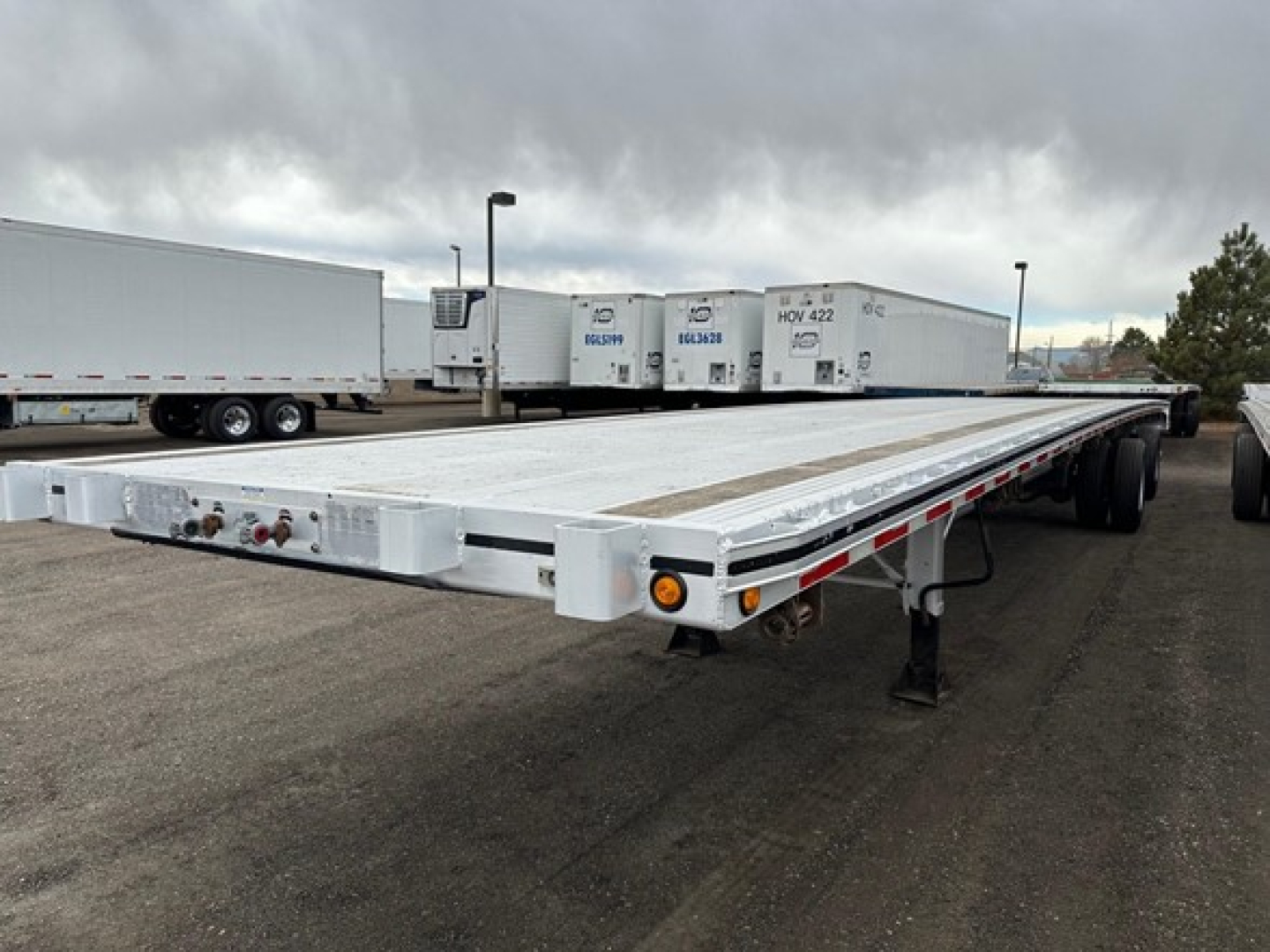 Flatbed trailer showing long aluminum deck with dual-axle rear, front jack, and side markers.