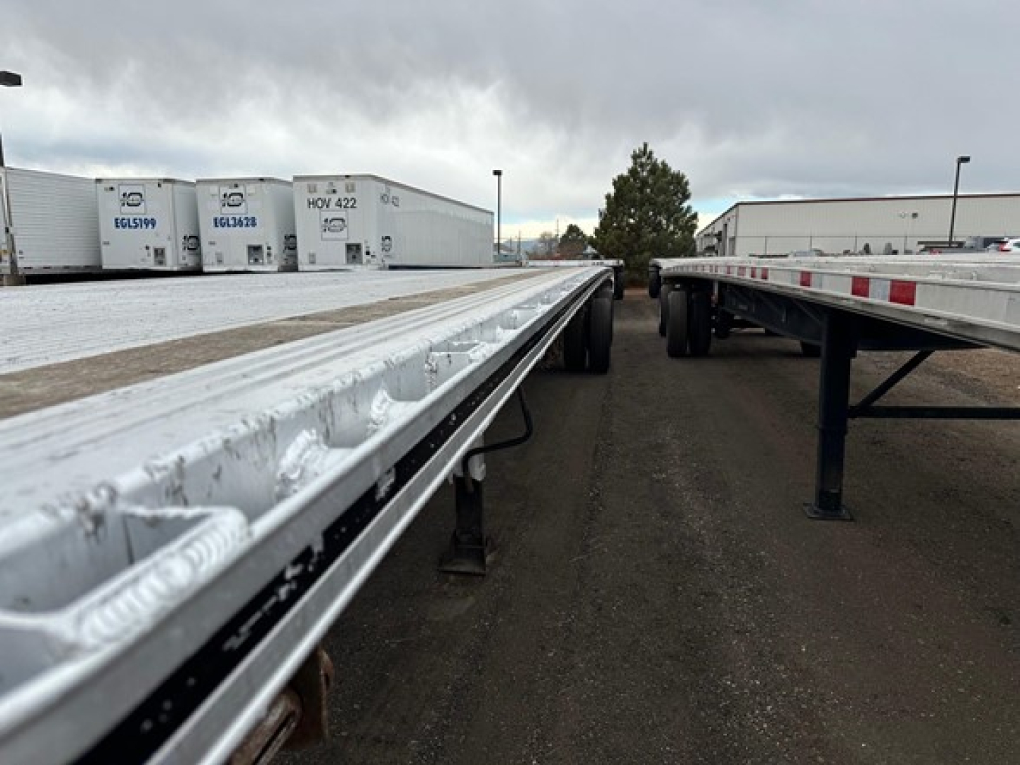 Aluminum flatbed trailer with reflective rim and dual-wheel setup, viewed from the side showing long aluminum deck sections and underslung support beams.
