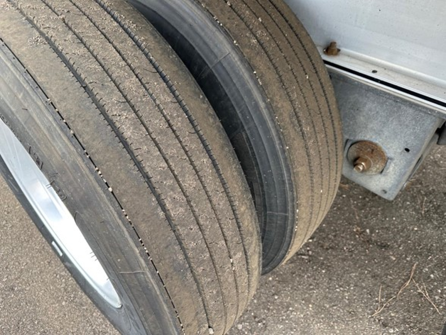 Flatbed trailer wheel area showing dual tires with tread and sidewall, aluminum frame edge, rust-free hardware.