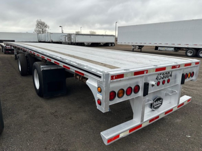 Flatbed trailer showing aluminum deck with dual rear axles and MAC Trailer logo on rear bumper; side and rear lights visible; VIN stock tag not legible.