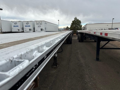 Aluminum flatbed trailer with reflective rim and dual-wheel setup, viewed from the side showing long aluminum deck sections and underslung support beams.