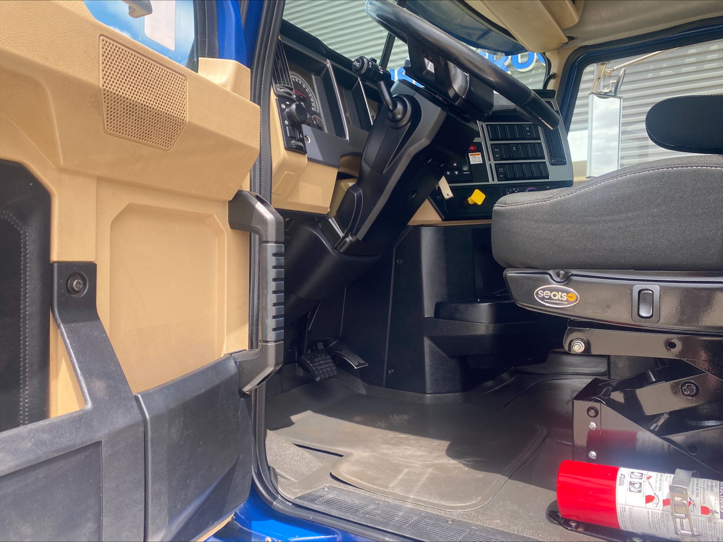 Truck cab interior of a 2019 Mack GR64F roll-off showing steering wheel, dashboard, and driver seat with Sealsco logo; tan panels and blue exterior visible.