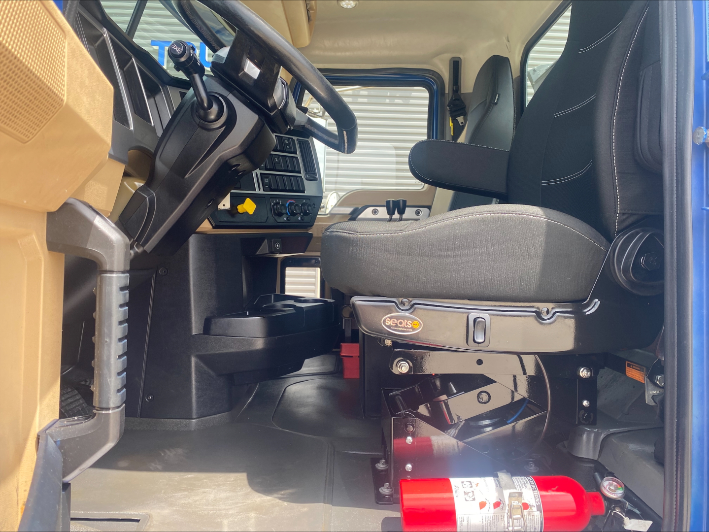 Cab interior of a 2019 Mack GR64F rolloff truck showing driver seat, steering wheel, and dashboard details.