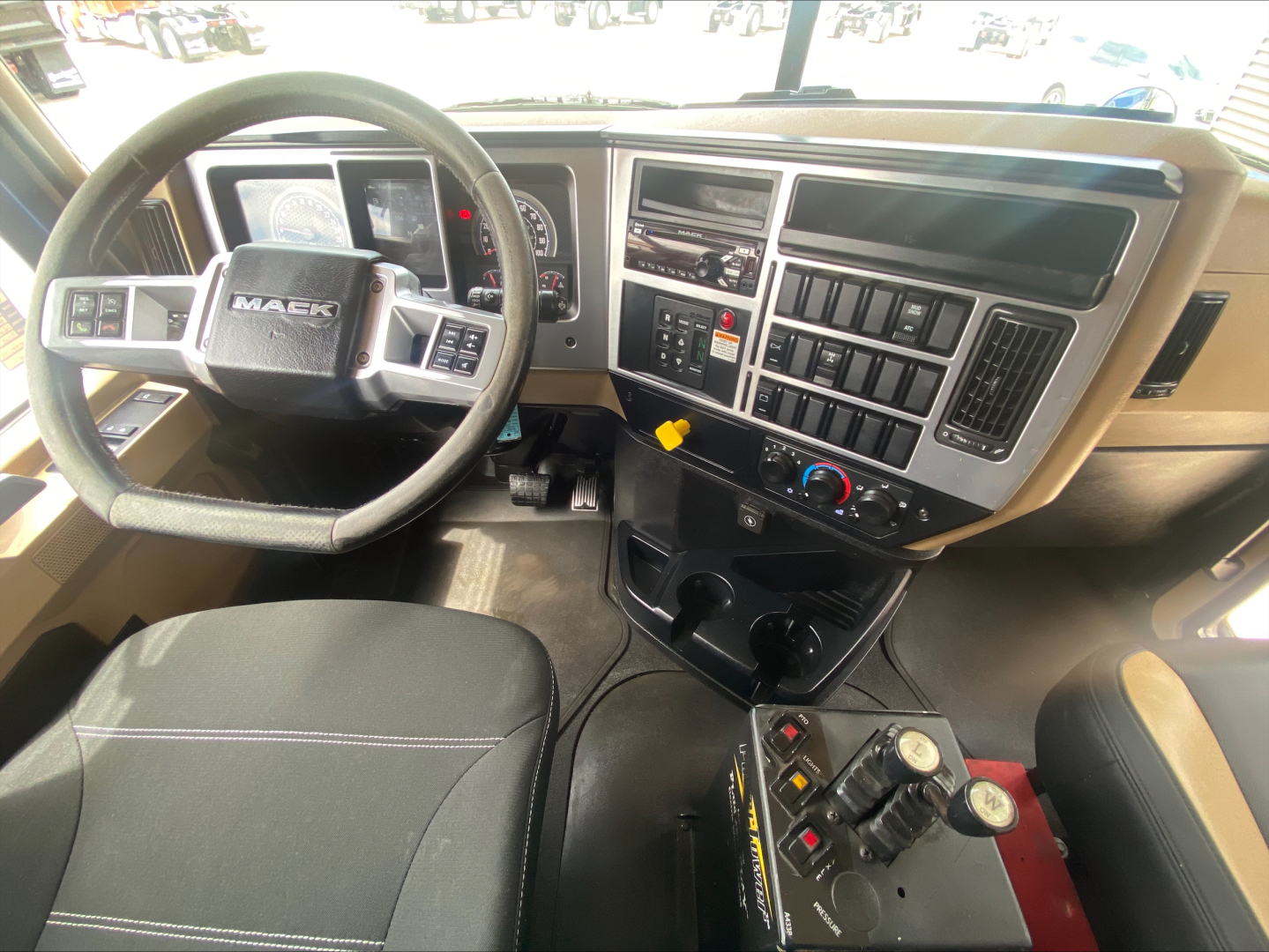 Cab interior of a 2019 Mack GR64F showing steering wheel, dashboard with digital gauges, control panel, gear selector area, and auxiliary controls.