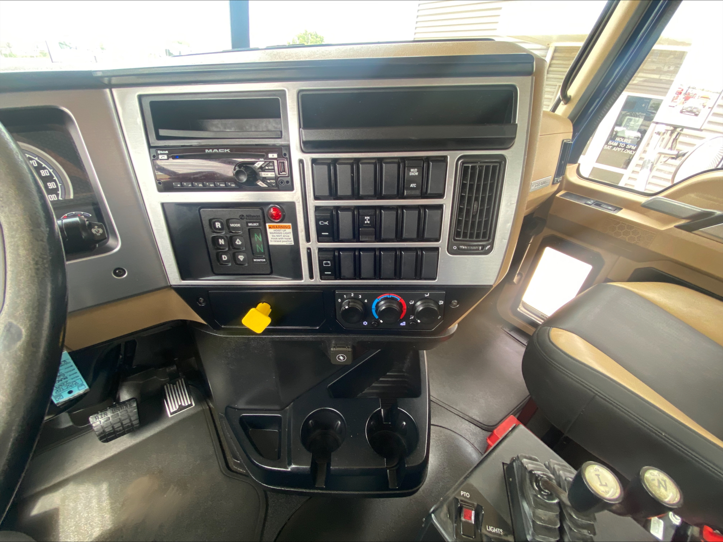 Mack GR64F cab interior showing dashboard controls, switches, cup holders, and steering column.