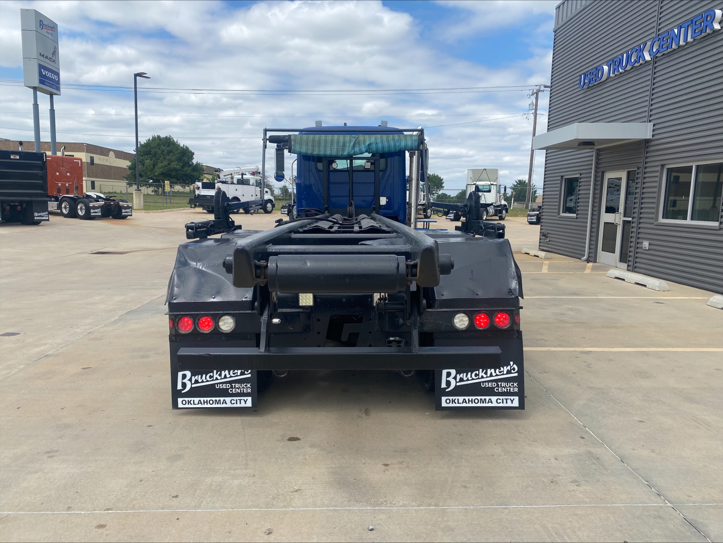 Back view of a 2019 Mack GR64F roll-off truck showing rear chassis, taillights, and mud flaps with Buckner’s Oklahoma City branding.