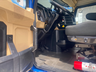 Truck cab interior of a 2019 Mack GR64F roll-off showing steering wheel, dashboard, and driver seat with Sealsco logo; tan panels and blue exterior visible.