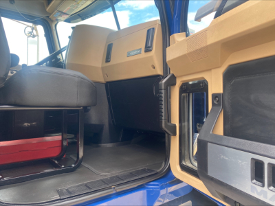 Truck cab interior of a 2019 Mack GR64F rolloff, tan dash panels, black seats, open door showing entry step and dashboard controls.