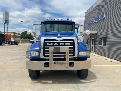 Front view of a blue 2019 Mack GR64F rolloff truck with chrome bumper, large grille, and chrome mirrors in a dealership lot.