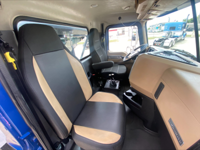 Mack GR64F cab interior showing beige and black seats, dashboard, and steering wheel in view.