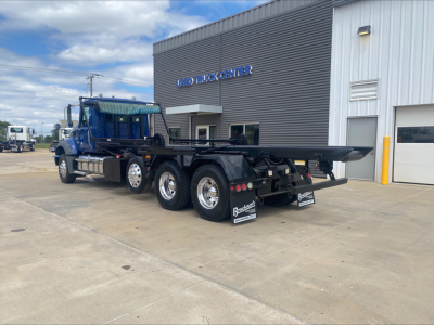 Truck chassis showing Mack GR64F flatbed in a lot with a blue cab and multiple axles.
