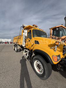 Mack CV713 dump truck in service showing front wheel and cab with yellow paint.