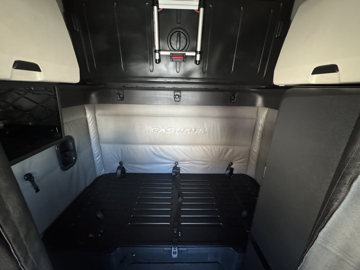 Freightliner Cascadia 126 truck interior cargo area with sleeper cabin, light gray upholstery, and black floor; branding reads 'CASCADIA' on back wall.