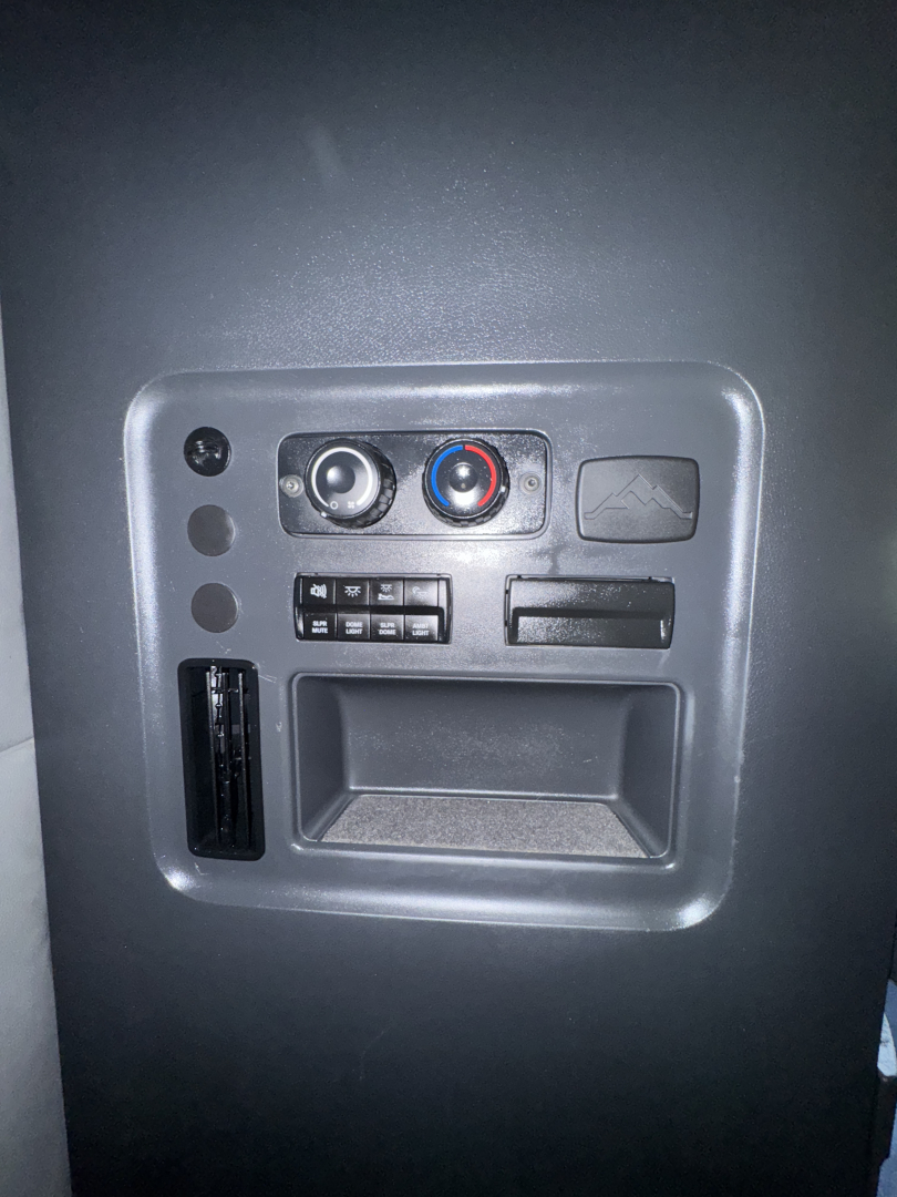 Dashboard area with circular climate control knobs, small panel switches, and a rectangular storage slot in a Freightliner Cascadia interior.