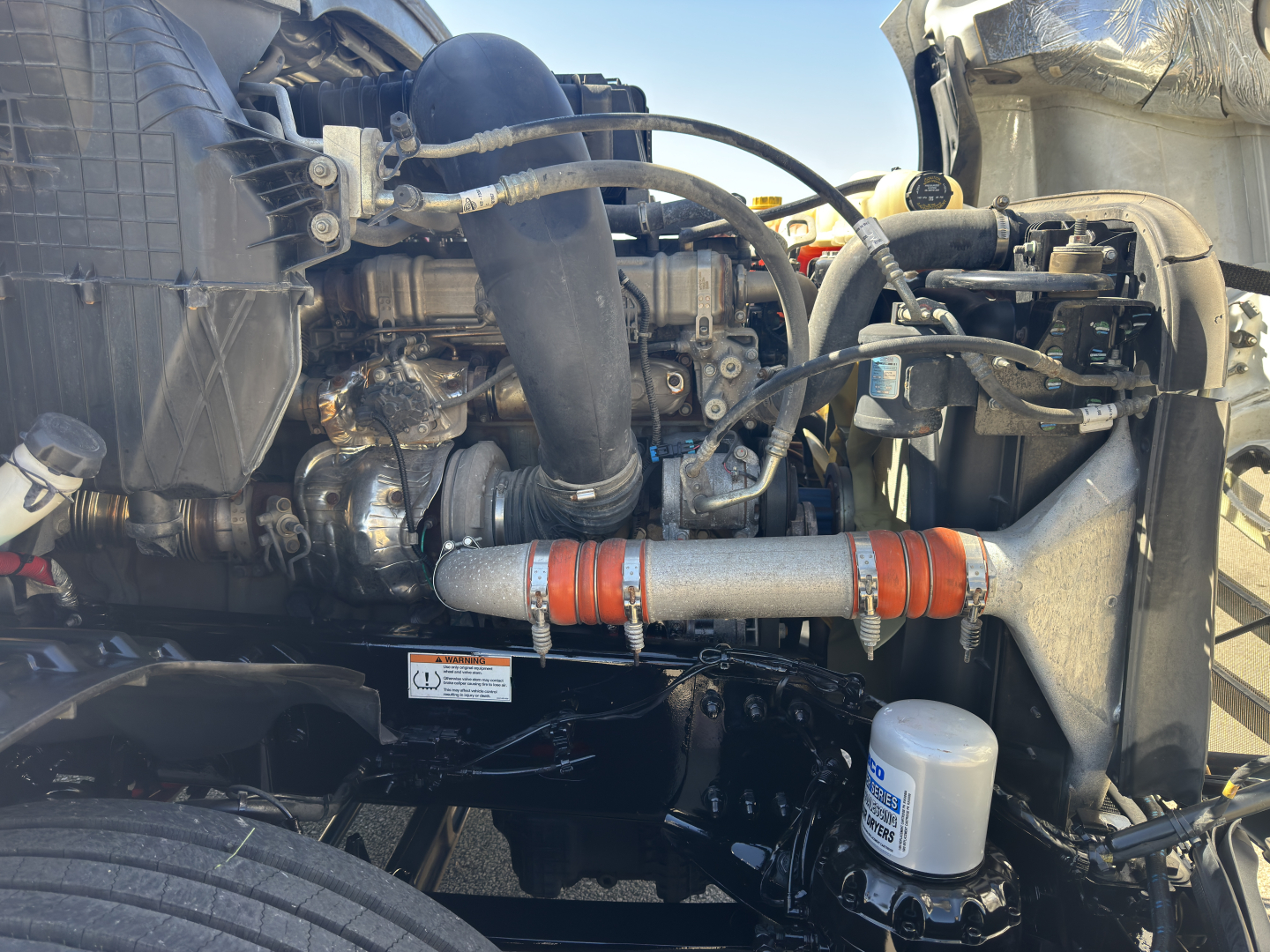 Freightliner Cascadia engine bay showing turbocharger piping and coolant hoses with orange insulated intercooler line and filter canister.