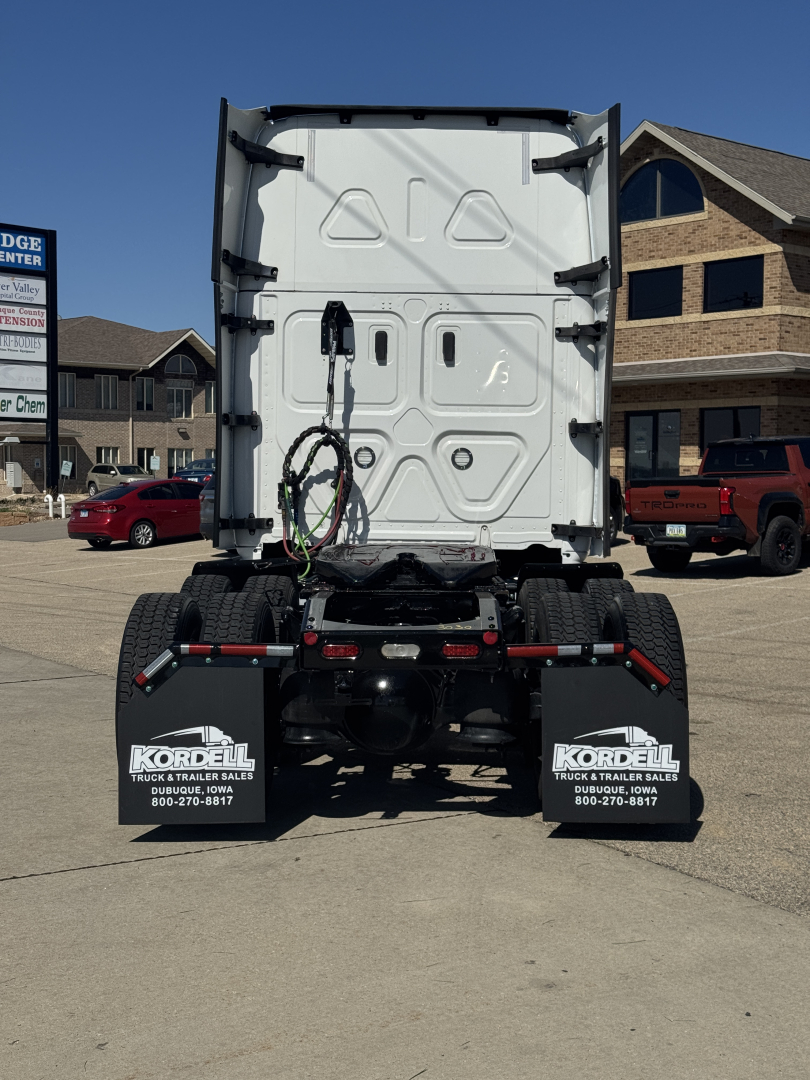 Rear view of a Freightliner Cascadia truck with fifth wheel, dual rear axles, and mud flaps showing Kordell truck sales contact numbers.