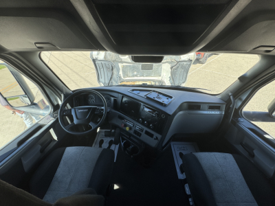 Cab interior of a Freightliner Cascadia truck with dashboard controls, steering wheel, and front seats visible through windshield.