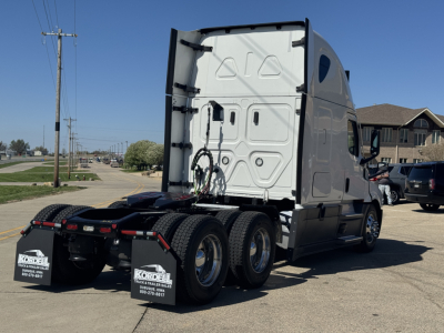  Freightliner Cascadia 126 tractor rear view showing dual rear axles and fifth wheel; white cab with sleeper, warning decals and mud flaps.