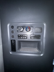 Dashboard area with circular climate control knobs, small panel switches, and a rectangular storage slot in a Freightliner Cascadia interior.