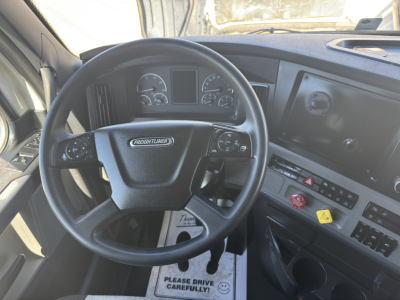 Freightliner Cascadia steering wheel and dashboard interior seen from driver seat showing steering wheel logo, instrument cluster, and control panel.