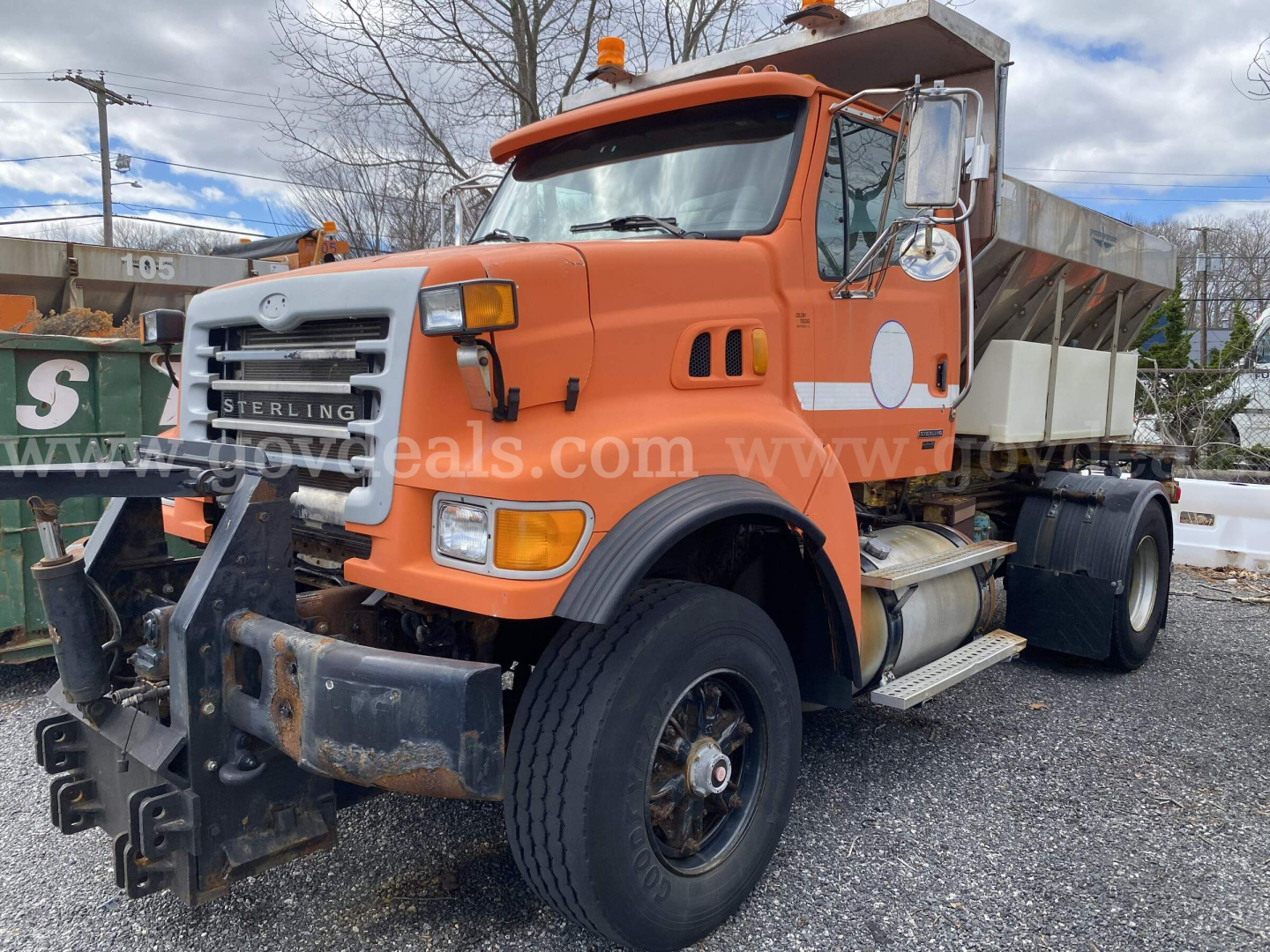 Dump truck showing Sterling L9500 front stance with orange cab and white dump bed. Visible text includes Sterling emblem on grille, wheel, and side steps.